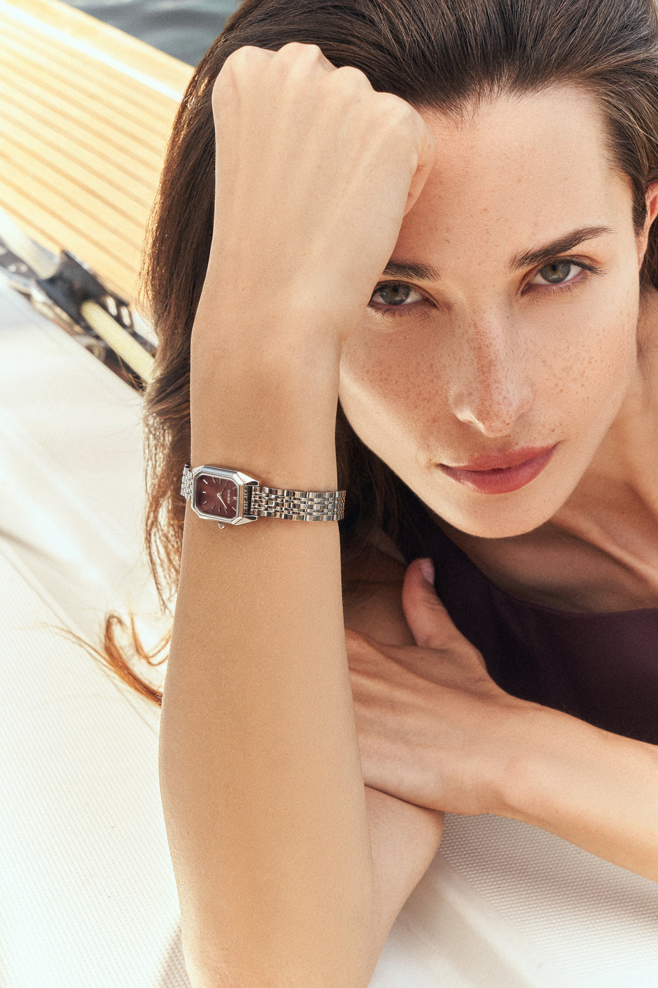 Woman wearing a rectangular silver-tone BURKER watch with a burgundy dial.