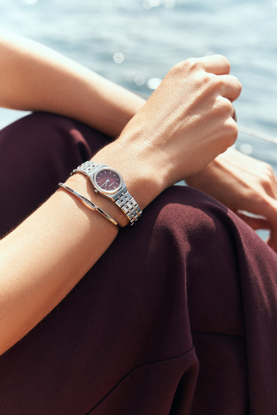 Silver-tone BURKER watch with a burgundy dial and a slim bracelet worn beside the water.