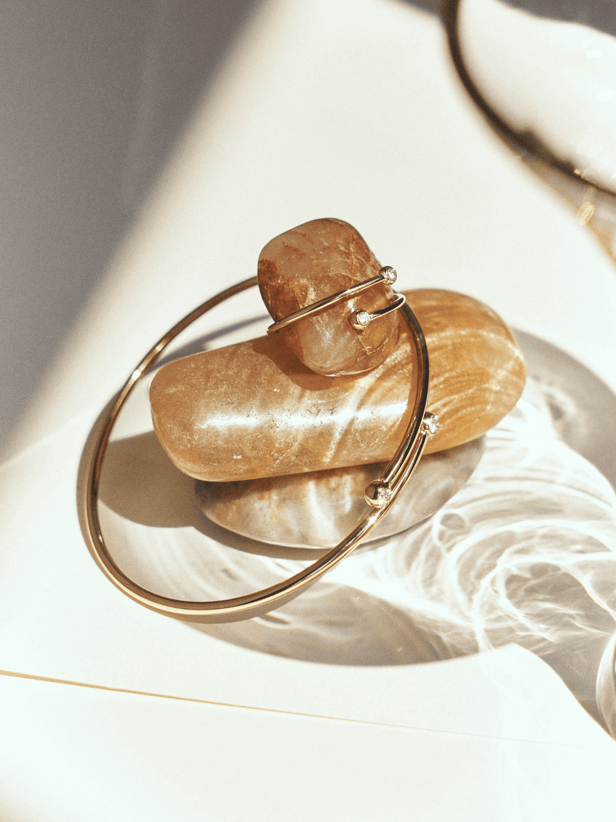 Gold-tone open bangle and matching ring with small stones, displayed on smooth pebbles.