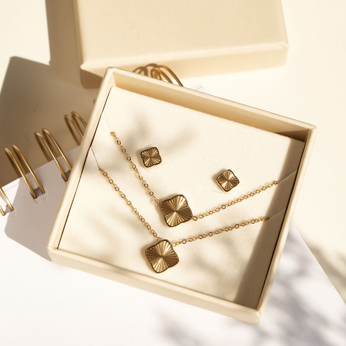 Gold-tone necklace, bracelet and square stud earrings displayed in a cream jewelry box.