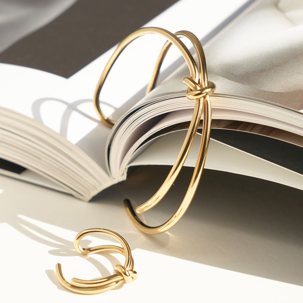 Gold-tone open bangle and matching ring with knot details, displayed beside an open book.