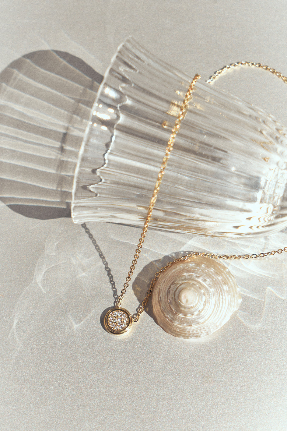 Gold-tone necklace with a round stone-set pendant draped over a clear glass.
