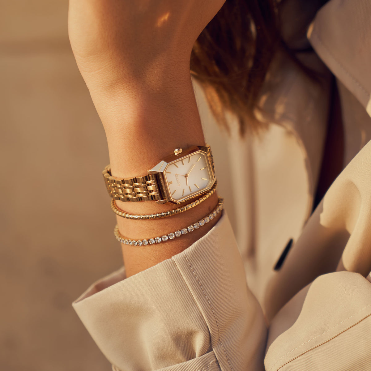 Gold-tone BURKER watch with a white dial, styled with slim bracelets and a cream shirt.