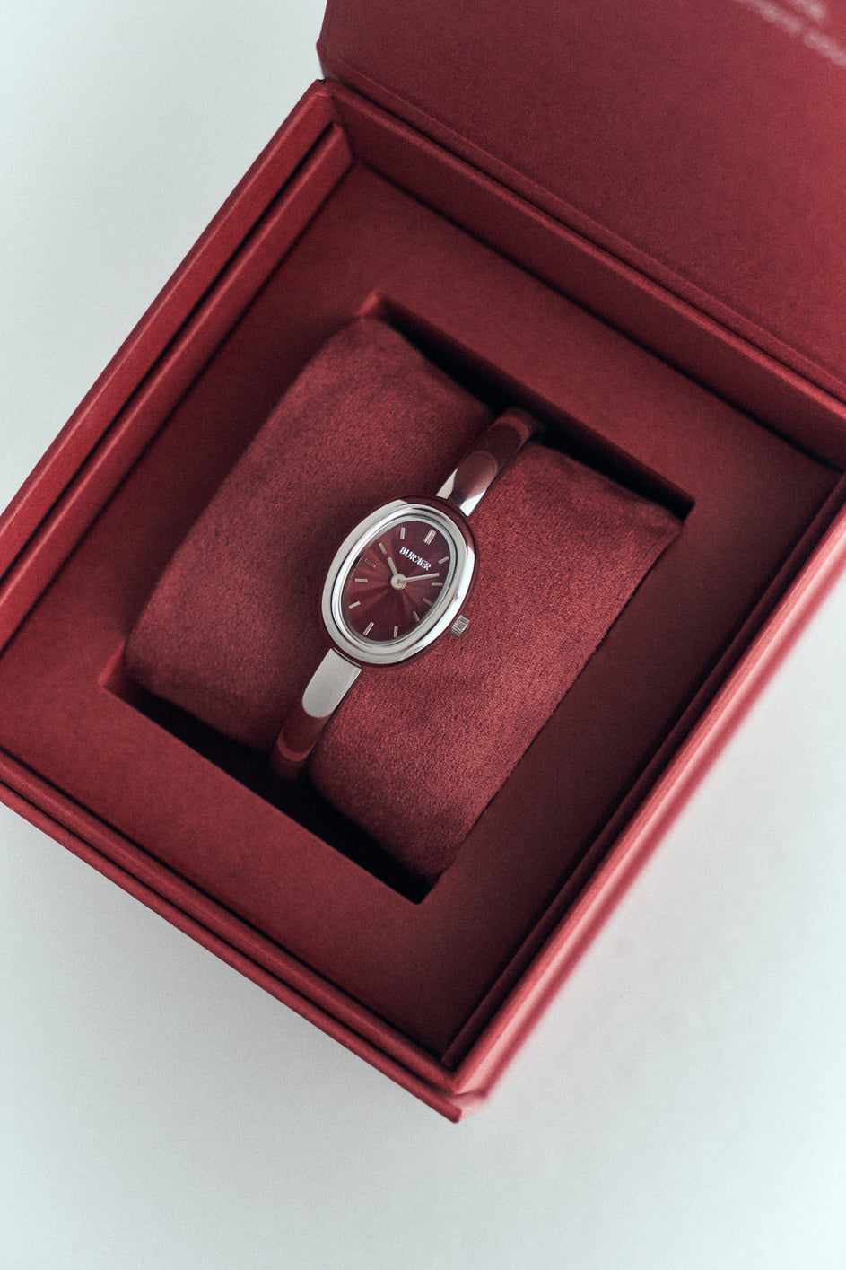 Silver-tone BURKER watch with an oval burgundy dial in a burgundy presentation box.